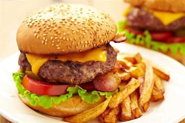 Cheese burger on a seeded bun with lettuce, tomato and pickles with fries