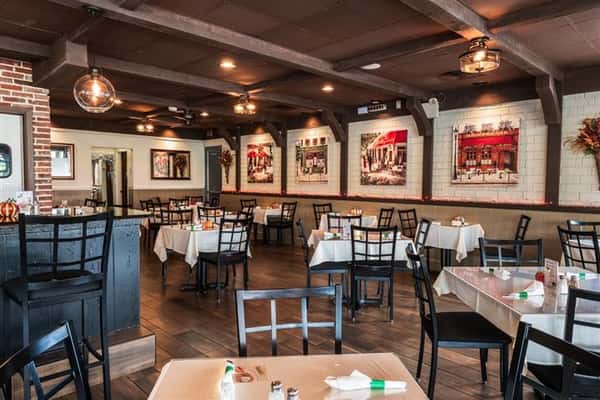 Dining area with wood floors, clothed tables, framed photos on walls