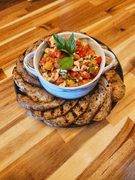 Heirloom bruschetta featuring a colorful mix of diced tomatoes, mozzarella, basil, and herbs, served in a ceramic bowl surrounded by grilled artisan bread slices.
