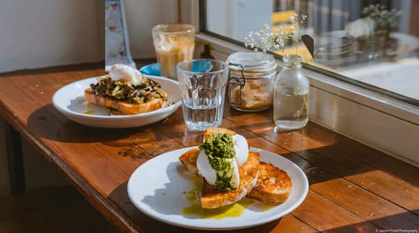 Poached eggs with pesto served on toast beside water and coffee on a wooden table.