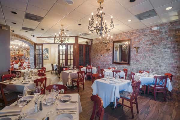 Elegant dining room with white tablecloths, red chairs, brick walls, chandeliers, and neatly set tables