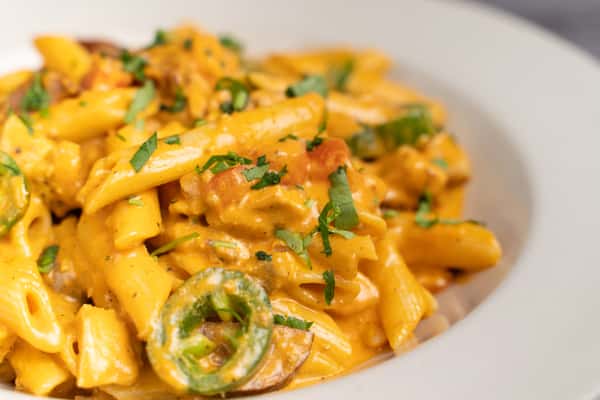 Creamy penne pasta with jalapeño slices, herbs, and savory sauce in a white bowl