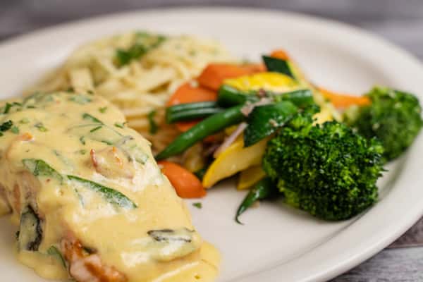 Grilled chicken breast topped with creamy herb sauce, served with pasta and mixed vegetables including broccoli and carrots