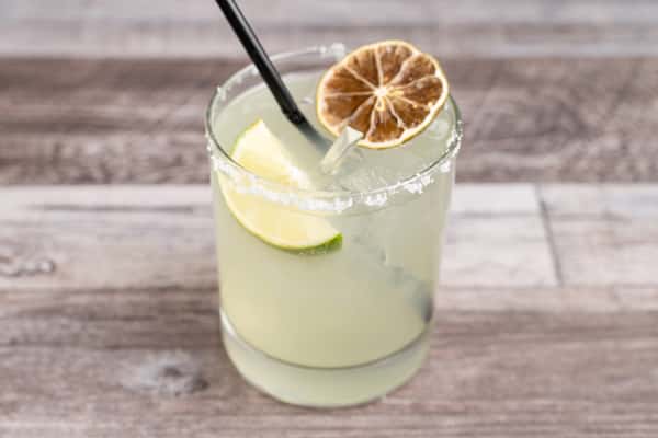 Salt-rimmed margarita with lime wedge and dried citrus slice in a rocks glass on a wooden table