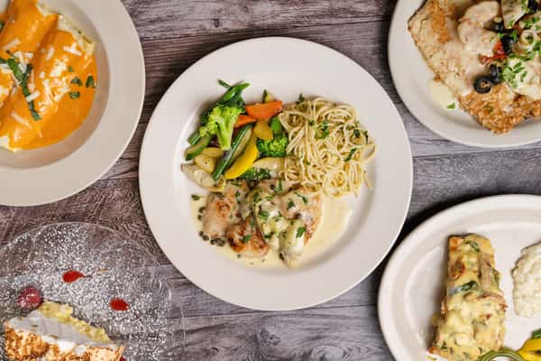 Overhead view of multiple plated dishes including chicken in cream sauce with pasta, vegetables, soup, and desserts