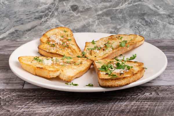 Four slices of toasted garlic bread topped with grated Parmesan and chopped parsley on a white plate