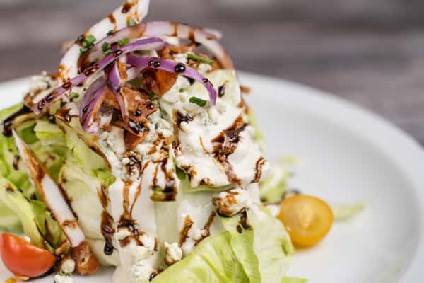 Wedge salad with iceberg lettuce, grilled chicken, blue cheese, bacon, red onion, and balsamic glaze drizzle
