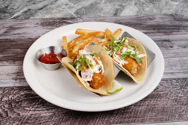 Two shrimp tacos topped with slaw and cilantro, served with fries, ketchup, and a lime wedge on a white plate