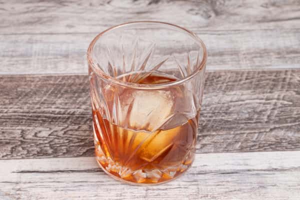 Old fashioned cocktail with large ice cube in cut crystal glass on rustic wood table
