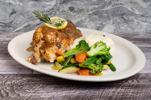 Roasted chicken with gravy, lemon and rosemary, served with mashed potatoes and mixed vegetables on white plate