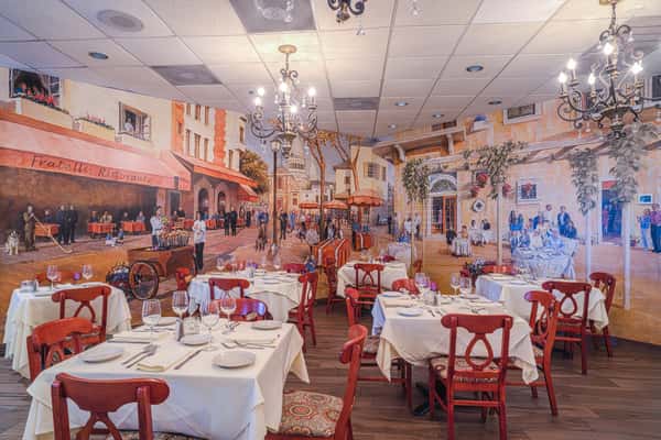 Elegant Italian restaurant interior with mural of a lively street scene, white tablecloth tables and red chairs