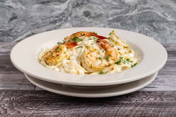 Grilled shrimp fettuccine Alfredo in creamy sauce, garnished with parsley, served in a white bowl