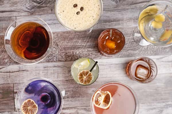 Overhead view of assorted cocktails on rustic table, including martini, espresso martini, old fashioned, and citrus drinks