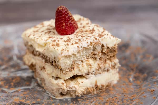 Tiramisu square dusted with cocoa powder, layered with mascarpone cream and topped with a fresh raspberry