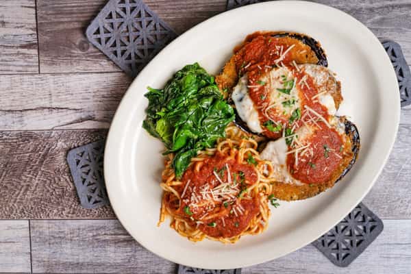 Chicken Parmesan with spaghetti marinara and sautéed spinach on a white plate over rustic wood background