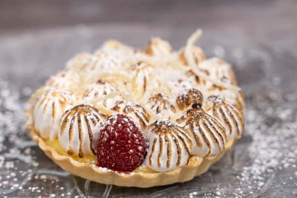 Mini lemon tart topped with toasted meringue peaks, shredded coconut, and a fresh raspberry dusted with sugar