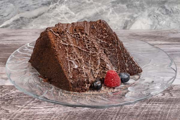 Rich chocolate bundt cake slice drizzled with chocolate ganache, served with fresh raspberries and blueberries on a glass dessert plate.