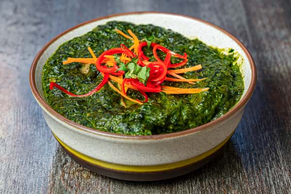 Palak paneer spinach curry garnished with sliced red chilies and herbs in a rustic bowl.
