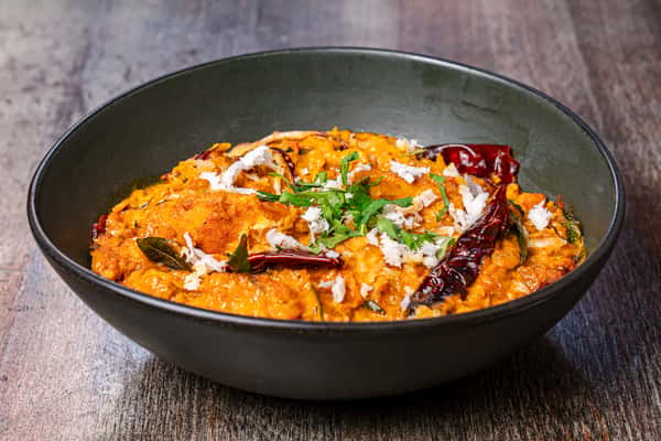 South Indian coconut chutney topped with dried red chilies, curry leaves, and grated coconut in a modern black bowl.