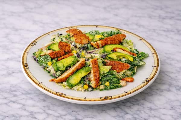 Fresh avocado toast topped with crispy seasoned shrimp and mixed greens on a marble tabletop.