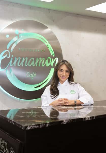Owner of Cinnamon Restaurant Café posing in front of the restaurant's illuminated logo, showcasing the welcoming spirit behind the dining experience.