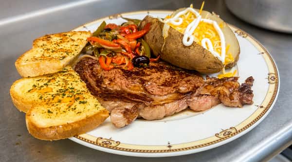 Grilled steak with sautéed peppers and onions, a loaded baked potato, and garlic bread on a white plate.