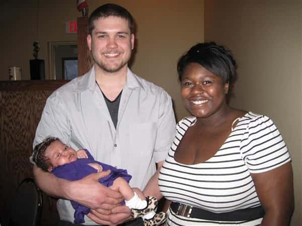 male and female smiling, male is holding a baby