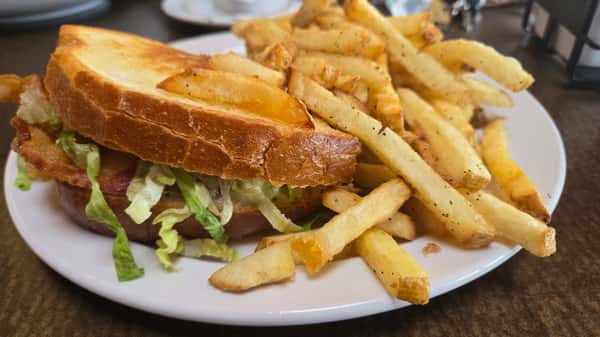 Toasted BLT sandwich with lettuce on thick bread, served with a generous portion of seasoned French fries.