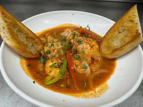 Sautéed shrimp in a zesty tomato-based sauce with bell peppers and onions, garnished with fresh herbs and served with toasted garlic bread.