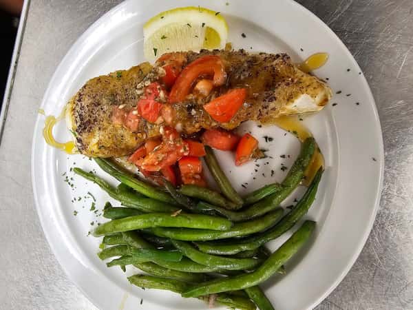 Seared fish fillet topped with diced tomatoes and sauce, served with green beans and a lemon wedge.