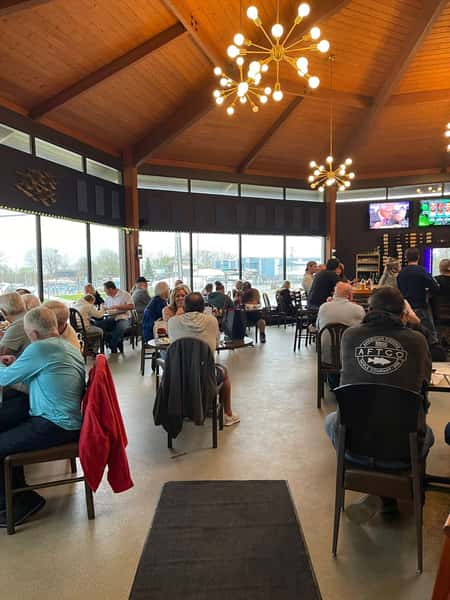 Busy restaurant dining room with high wooden ceilings, modern chandeliers, and guests seated at tables enjoying meals.