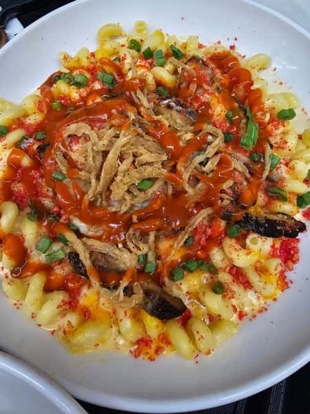 Creamy macaroni and cheese topped with crispy fried onions, green onions, hot sauce, and crushed red seasoning.