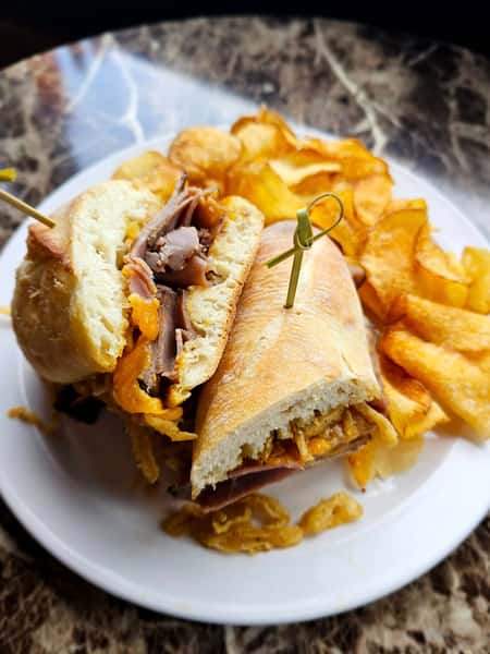 Toasted sandwich filled with roast beef, cheddar cheese, and crispy onions, served with a side of kettle chips on a white plate.