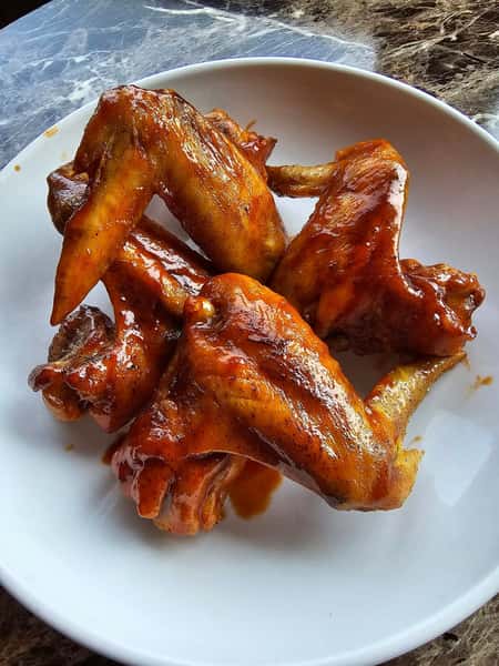Crispy chicken wings coated in a glossy, spicy barbecue sauce served in a white bowl.
