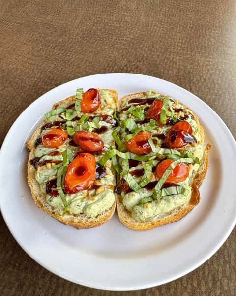 Toasted bread topped with creamy pesto spread, blistered cherry tomatoes, shredded basil, and a drizzle of balsamic glaze.