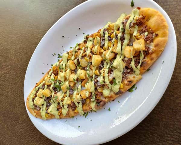 Flatbread topped with seasoned beef, roasted corn, diced potatoes, herbs, and drizzled with a creamy green sauce.