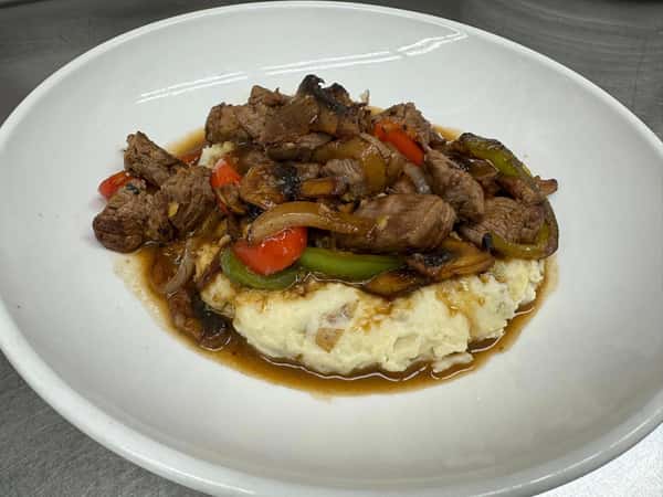 Seared beef tips with sautéed onions and peppers over a bed of creamy mashed potatoes, topped with savory brown gravy.