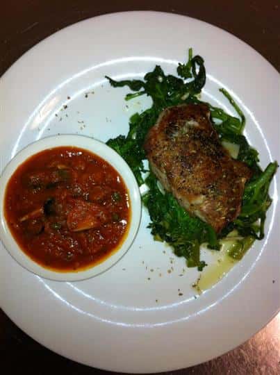 Meat cutlet over a bed of sauteed greens and served with a side of red sauce mixed with vegetables