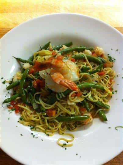 Seafood pasta dish with spaghetti tossed with vegetables and two shrimps on top