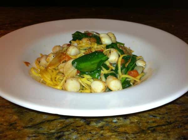 Fettuccine pasta tossed with scallops and basil leaves served in white deep dish