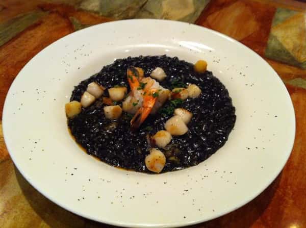 Sauteed Scallops served with black pasta in a white plate sprinkled with black pepper