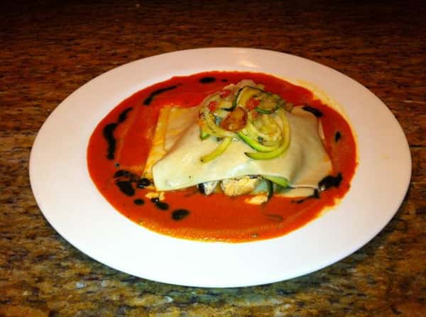 Lasagna dish with vegetables on top for garnish smothered in red sauce