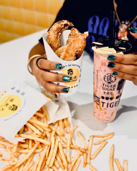 Person holding crispy chicken tenders from Chunky Boss and a pink Tiger Sugar bubble tea, with a large pile of fries on the table.