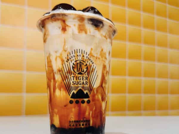 Tiger Sugar brown sugar boba drink with creamy swirls and tapioca pearls, set against a yellow tiled background.