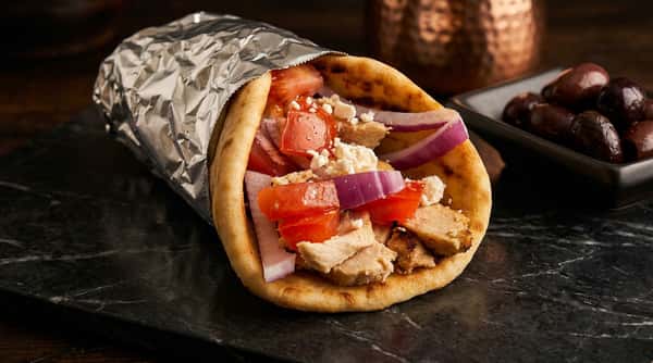 Chicken gyro in pita bread with red onions, tomatoes, feta cheese, and tzatziki sauce, partially wrapped in foil.