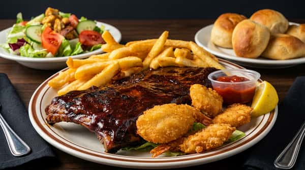 BBQ ribs with french fries, fried shrimp, a lemon wedge, and ketchup on a white plate.