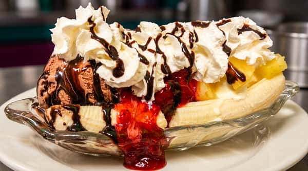 Banana split with chocolate, vanilla, and strawberry ice cream, whipped cream, chocolate syrup, and fruit toppings.