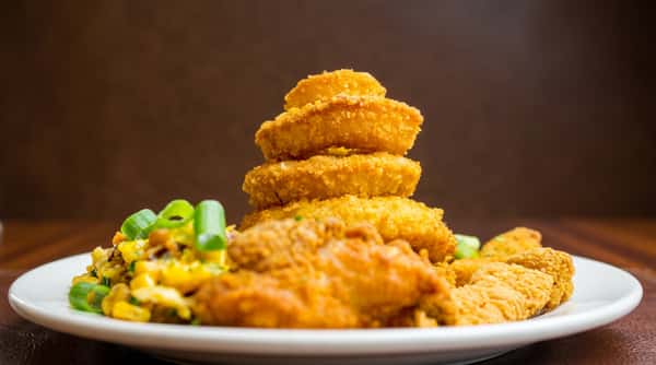 Golden-brown fried chicken nuggets and onion rings stacked on a white plate, with chopped green onions.