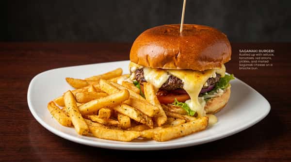 Saganaki Burger with melted cheese, tomato, lettuce, and a side of french fries on a white plate.