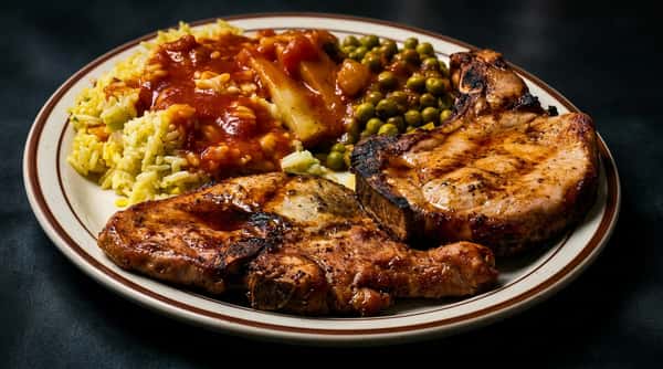 Plate with two grilled pork chops, yellow rice with tomato sauce, and green peas with stewed vegetables.
